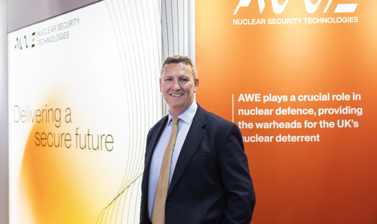 AWE's CEO smiles, standing in front of an orange and white exhibition stand