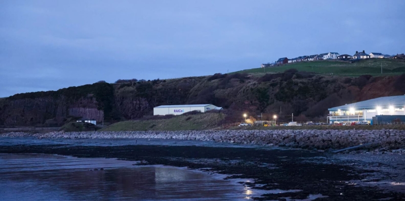 A building with the word RAICo on it against a backdrop of hill cliffs and a beach