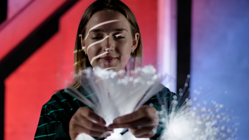 A person holds glowing fiber optic cables against a red and blue gradient background with black diagonal lines.