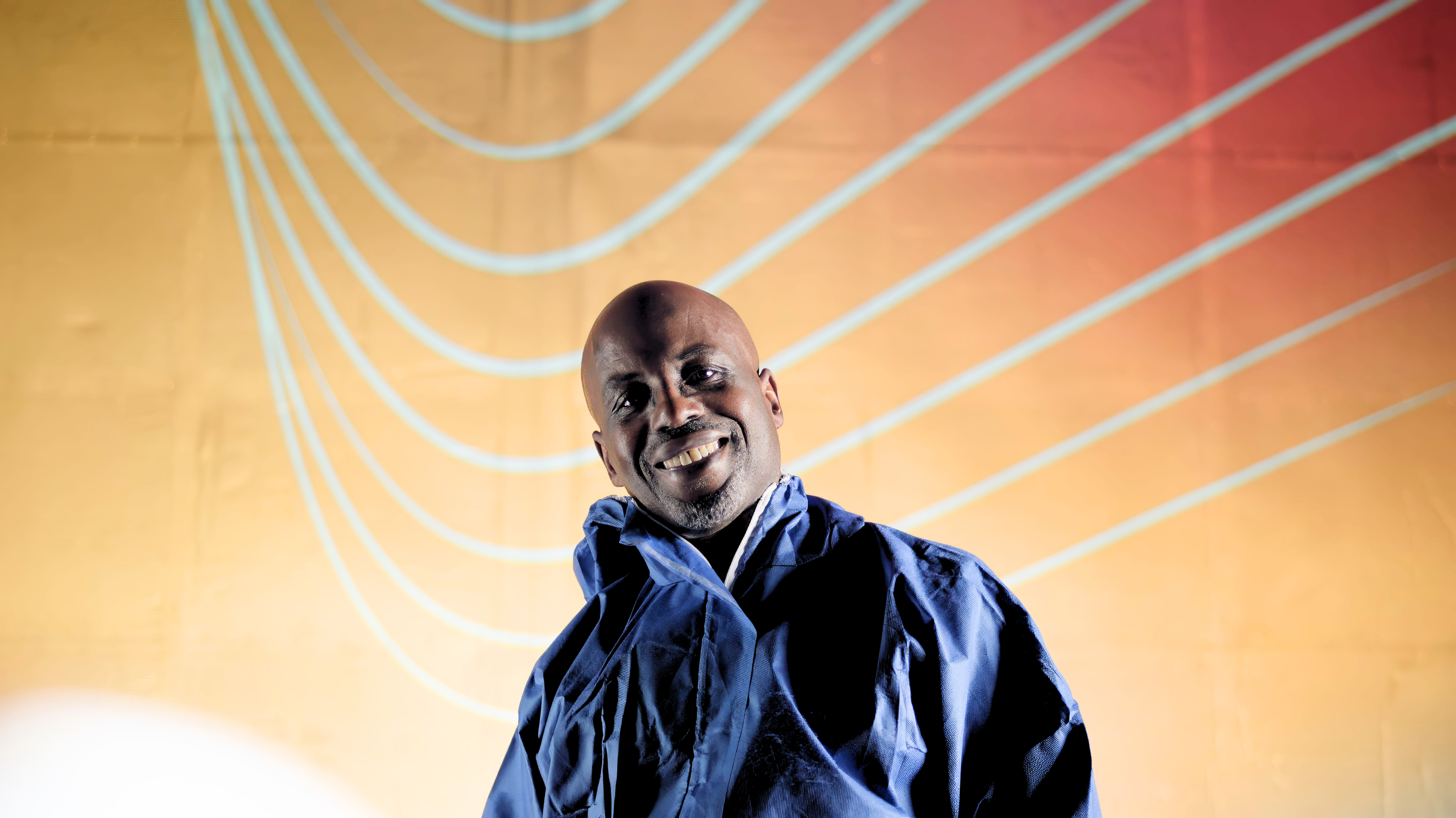 Person in a blue protective suit and black gloves holding a virtual reality headset above their head, with curved illuminated lines in the dark background.