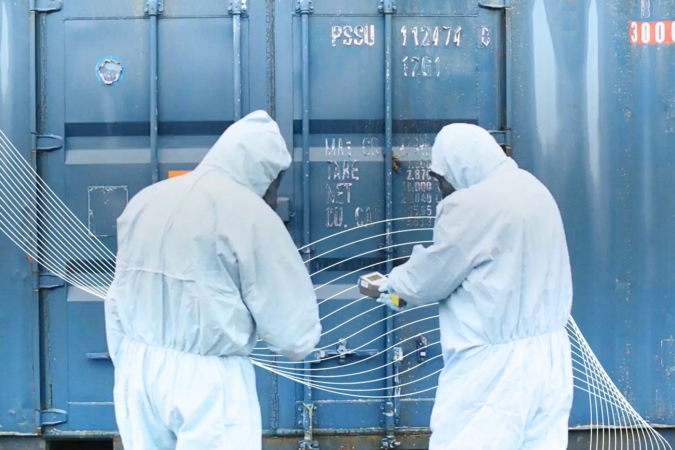 Two people in white hazmat suits and PPE test for radiactivity.