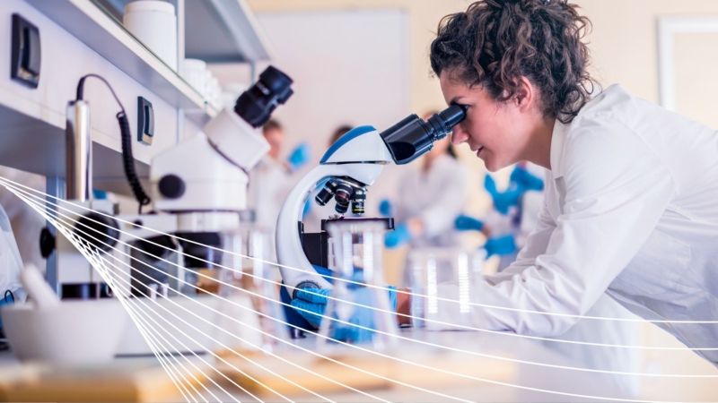 rainee in a white lab coat examines samples under a microscope in a research lab filled with scientific instruments and glassware, illustrating hands-on training in nuclear materials analysis.