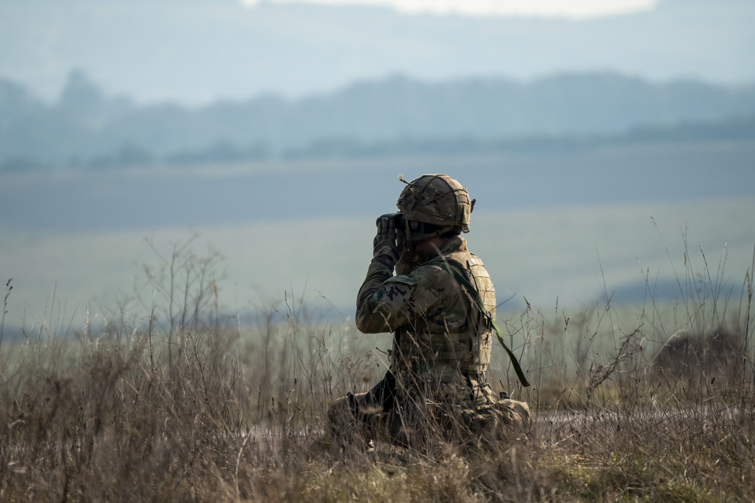 close-up of a British army infantry soldier using binoculars to scan distance for enemy threats, military exercise, Wiltshire UK
